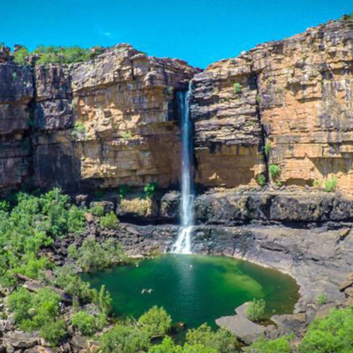 Waterfall entering a green pool amongst red cliffs