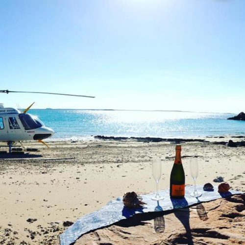 Salty Wings helicopter on a beach near a picnic rug and champagne