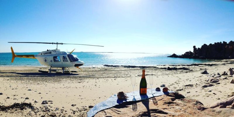Salty Wings helicopter on a beach near a picnic rug and champagne