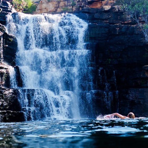 A woman swimming in a pool beneath a waterfall