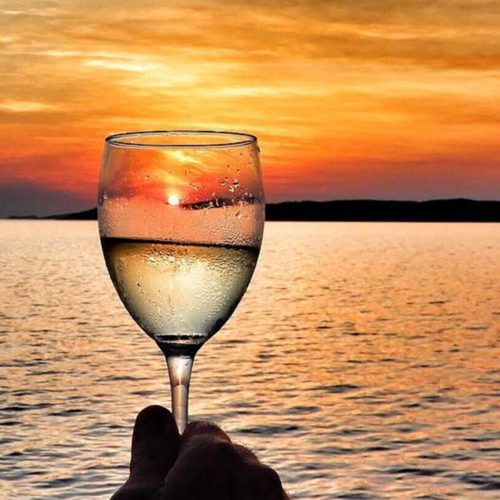 Glass of white wine held before a sunset landscape
