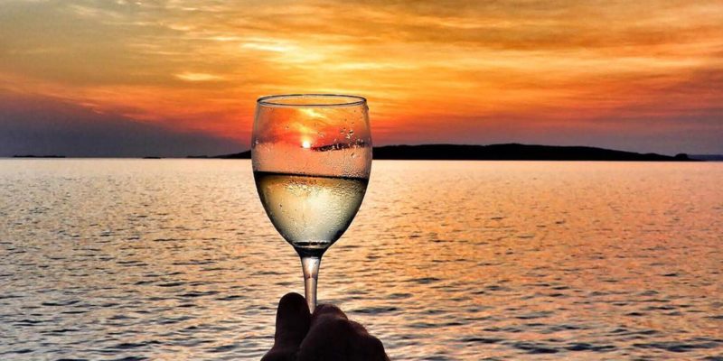 Glass of white wine held before a sunset landscape