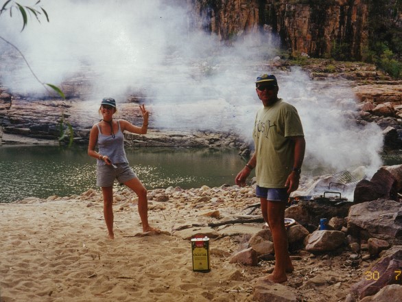 Two people posing for the camera in front of a smoking campfire