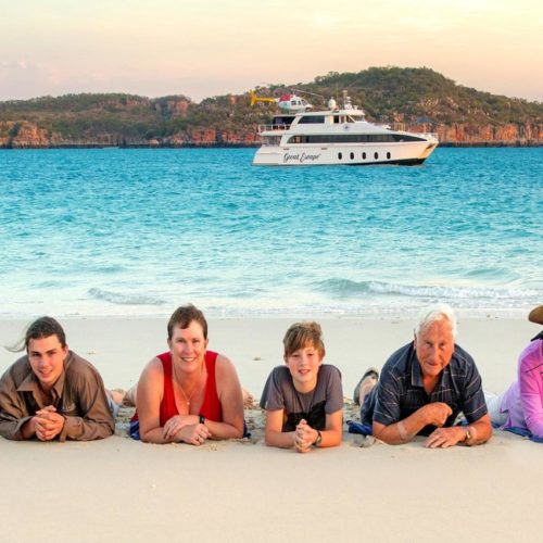 Extended family members lying on beach with Great Escape Cruise Charter in the background